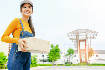 Smile friendly female employee beautiful asian yellow uniform online parcel delivery service unloading parcels loading boxes goods delivery service customer's address standing in front of the village.