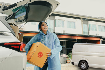 Asian businesswoman driving delivery running business online ordering wholesale retail online logistics wearing raincoat delivering parcel boxes in the rainy season to customers in front of the house.