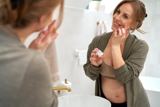 Caucasian pregnant woman doing skincare in the bathroom