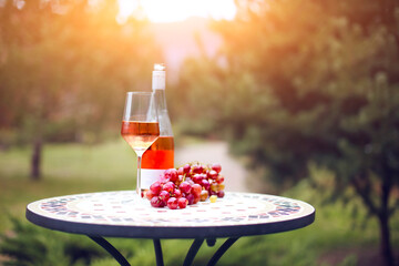 One glass and bottle of rose wine in autumn vineyard on marble table.
