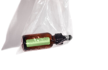 Brown essence or serum glass bottle with a dropper is in transparent plastic bag. Mockup with green sticker on bottle on white background.
