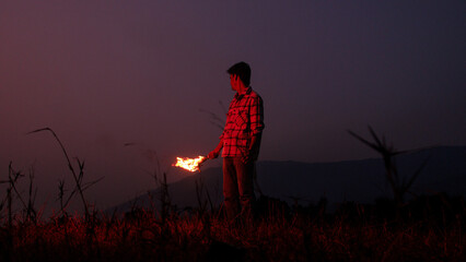 Image of brave man holding burning stick while moving in darkness. Young man holding a fire stick...