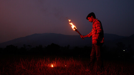 Image of brave man holding burning stick while moving in darkness. Young man holding a fire stick on the mountain top near the sea. - Powered by Adobe