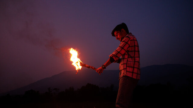 Image of brave man holding burning stick while moving in darkness. Young man holding a fire stick on the mountain top near the sea.