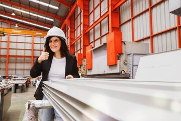 Female manager engineer inspects the quality white coated rolled metal roofing sheets in a standardized and safe warehouse production facility showing thumbs up on product quality.