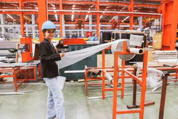 Female inspection engineer inspects the quality of plastic rolls, galvanized sheets, metal sheets in an industrial factory with confidence, trusting the quality of the materials during production.