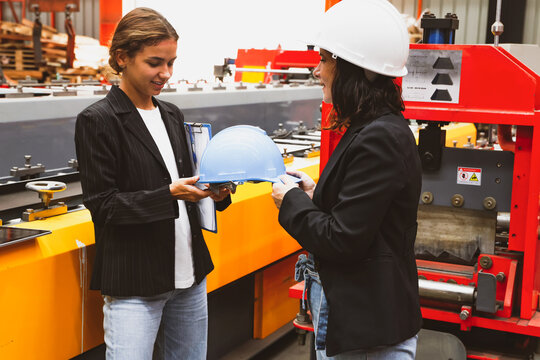Female factory manager gladly handed over safety helmet while taking female business woman and business partner on a tour of the production work area in the metal sheet industry to ensure safety.