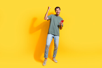 Full length photo of funny lucky man dressed khaki t-shirt winning game apple iphone samsung modern gadget isolated yellow color background