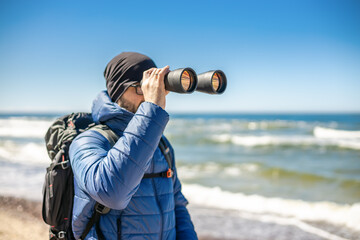 Obraz premium A tourist man standing by the seashore, looking through binoculars