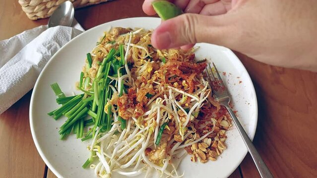 Squeezing kaffir lime over a plate of thai stir-fried rice noodles or pad thai, a famous iconic dish from Thailand 