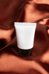 Cosmetic product in tube, bottle, lotion or serum on shiny cloth background