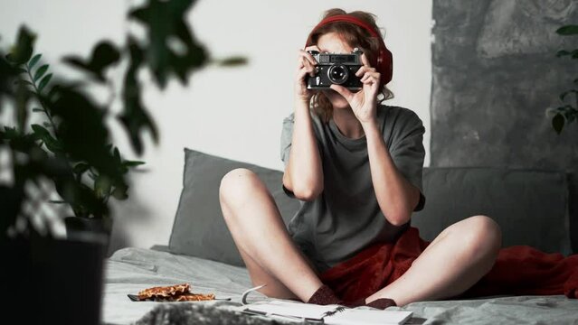 A young woman on a soft sofa at home takes pictures with an old vintage film camera. A full-length portrait.