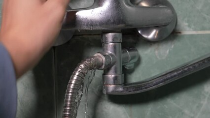 Close-up of man's hand holding damaged, old, rusty, leaking water faucet hose in bathroom. Concept of plumbing problem and faucet repair need. Plumber