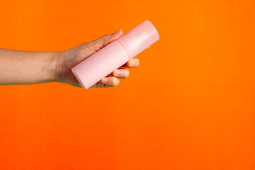Cosmetic pink bottle. Womens cosmetic accessory and hand for makeup on orange background.