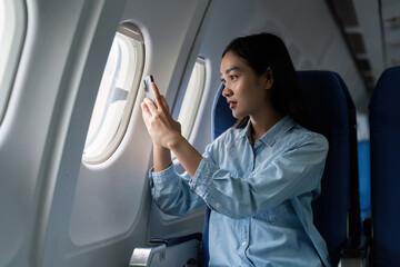 Asian people female person onboard, airplane window, using mobile while on the plane
