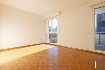Empty room with white walls and parquet. There is a window overlooking nature.