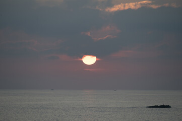 Tramonto sul mare con il sole in parte nascosto dalle nuvole.