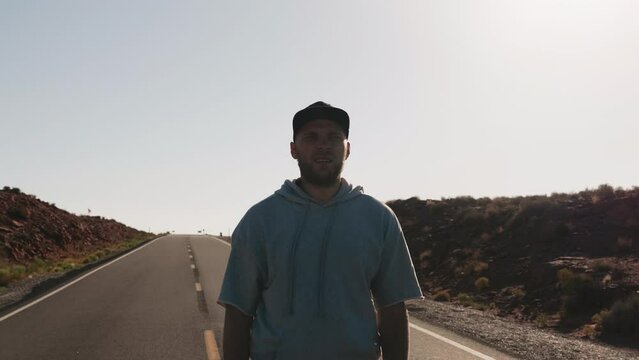 Camera zooms in on young amazed and excited man on highway looking at epic cinematic sunny sandstone desert of Arizona.