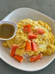 Omelette with pork bacon cutted on rice and sauce on white ceramic plate and spoon and fork. 