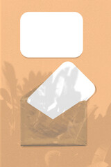 An envelope with two sheets of textured white paper on orange background. Natural light casts shadows from the leaves of a tree branch. Mockup vertical orientation.