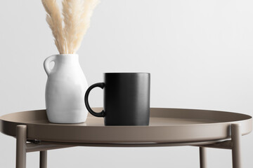 Black mug mockup with a pampas decoration on the beige table.