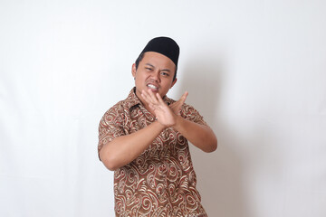 Portrait of excited Asian man wearing batik shirt and songkok  showing X sign of hands, refusing an...