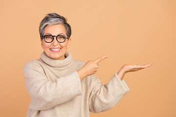 Portrait of cheerful pretty lady toothy smile direct finger arm hold empty space isolated on beige color background