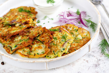 Zucchini fritters with red onions, garlic and herbs. Vegetarian zucchini pancakes and sour cream on white table.