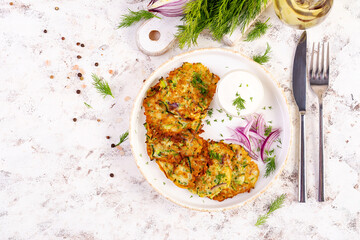 Zucchini fritters with red onions, garlic and herbs. Vegetarian zucchini pancakes and sour cream on white table. Top view