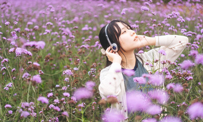 Obraz na płótnie Canvas Portrait of young adult asian woman relax in wild flower listen music with headphone and dancing in self mood