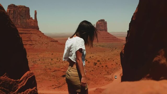 Back view young attractive woman stands between two giant rocks at amazing desert vista point of Monuments Valley posing