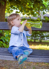 Cute little toddler boy drinking water from a big green bottle in the park, hydrating properly in hot summer day