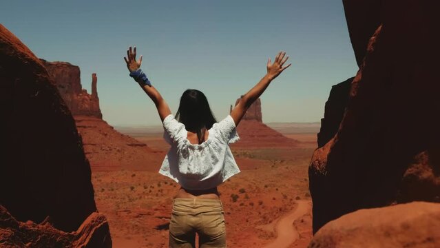 Back view young happy tourist woman standing at epic desert vista point arms wide open at Monuments Valley Arizona USA.