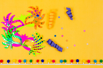 Two colorful paper carnival masks on a yellow background decorated with confetti.