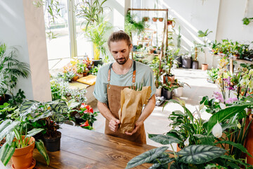 Handsome man wearing apron wrapping a potted plant in paper.