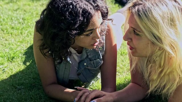 video of two young lesbian girls smiling lying face down on the grass holding hands talking