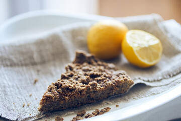 Side view of a piece of healthy, organic, sugar-free, gluten-free, dairy-free dessert served with lemons with copy space. Homemade healthy dessert with two lemons on the grey fabric. Selective focus