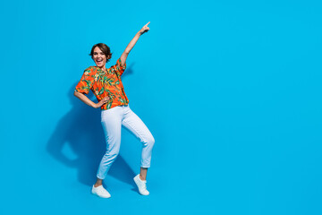 Fototapeta na wymiar Full size photo of cheerful nice girl dancing point finger empty space ad isolated on blue color background