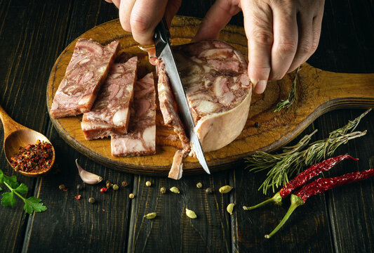 The chef, with a knife in his hand, cuts the brawn into pieces on the kitchen board before preparing delicious sandwiches. Fast street food concept.