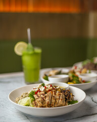 Delicious gourmet healthy chicken salad bowls and fresh mint margherita, with Spanish onion, lettuce, lemon and olive oil, served in white ceramic bowl, with seasoning and herbs on a restaurant table.