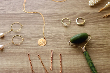 Pearl headband and barrette, golden eyeglasses, gold necklace, earrings and rings, jade face roller and hair pins on wooden background. Various elegant gold accessories. Selective focus.
