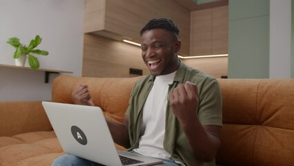 Positive Vibes as a black man reads heartening news on his laptop, basking in the comfort of home. A moment of positivity and celebration in daily living.