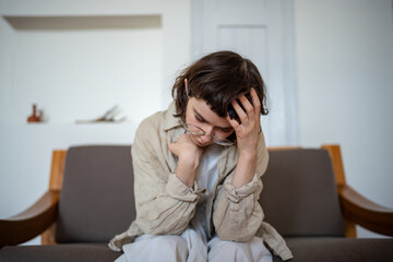 Stressed unhappy teenager sitting on bed, looking at floor. Unhappy teen has awkward age problems,...