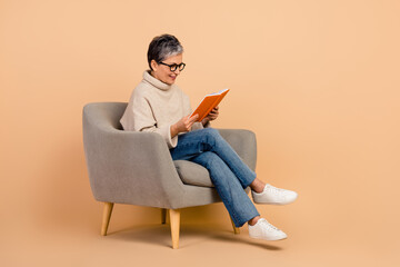 Full body length photo of intelligent elderly woman has hobby reading book when sitting on armchair...