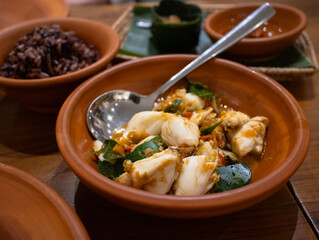 A plate of Thai spicy stir fry lump crab meat with chili and garlic, herbs, green lime leaves with black rice cooked in background