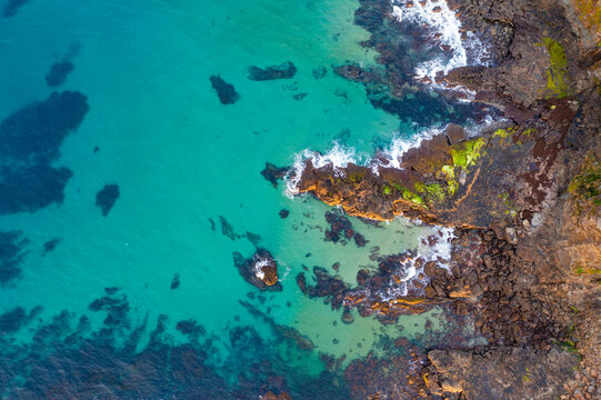 Aerial view of gentle waves washing onto rocks along the edge of calm turquoise sea