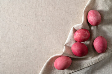 Pink colored Easter eggs on neutral beige linen tablecloth and napkin background with soft natural sun light and shadow, top view, flat lay, empty copy space