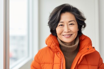 Portrait of a glad asian woman in her 50s sporting a quilted insulated jacket against a modern minimalist interior. AI Generation