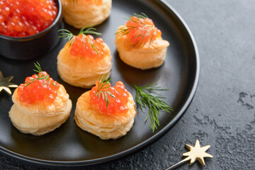 Salmon red caviar toast. Christmas canape or toast with red caviar on black plate on dark background. Idea to xmas snack. Gourmet food. Texture of caviar. Seafood.