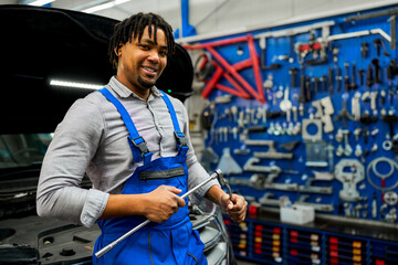 An African-American mechanic confidently posing with tools in hand in his workshop.